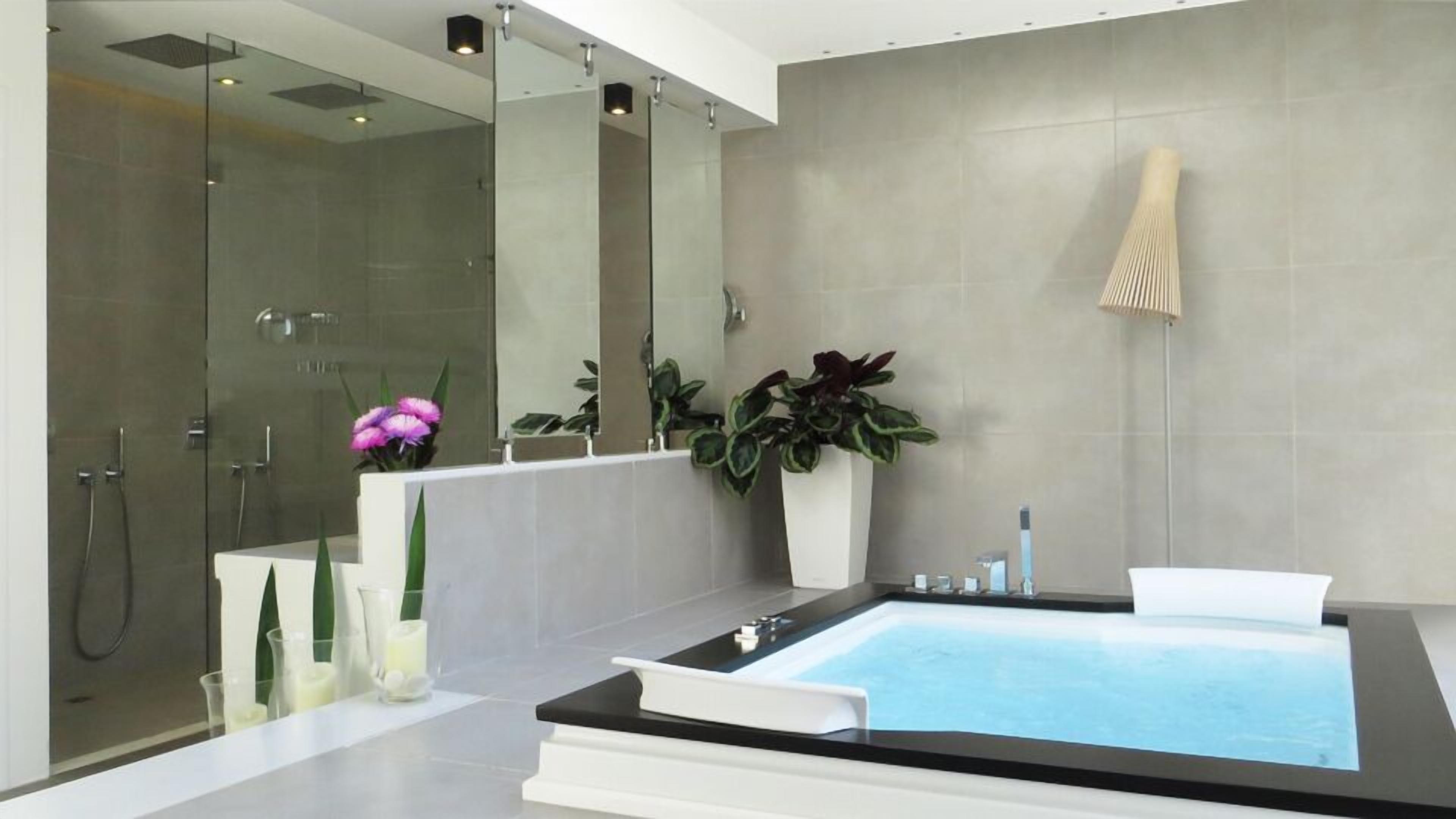 A modern bathroom with a glass-enclosed shower, a large bathtub, and potted plants.
