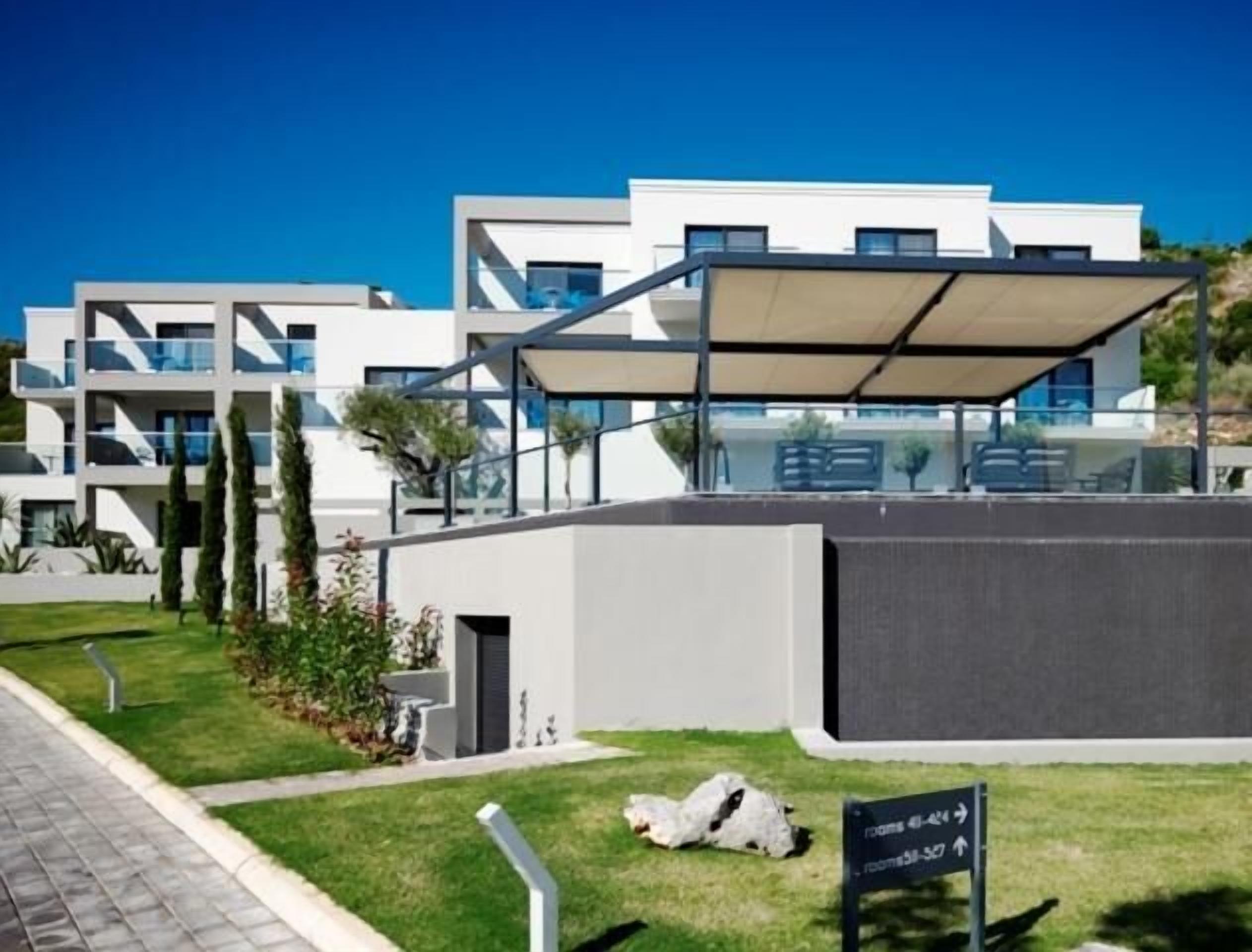 A modern building with a glass facade, a covered outdoor seating area, and a sign indicating room numbers.