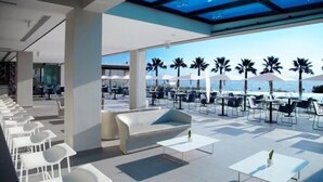 A modern outdoor seating area with a pool view, featuring white tables and chairs, a sofa, and umbrellas. - Tesoro Blu Hotel & Spa - Adults Only (Kefalonia)