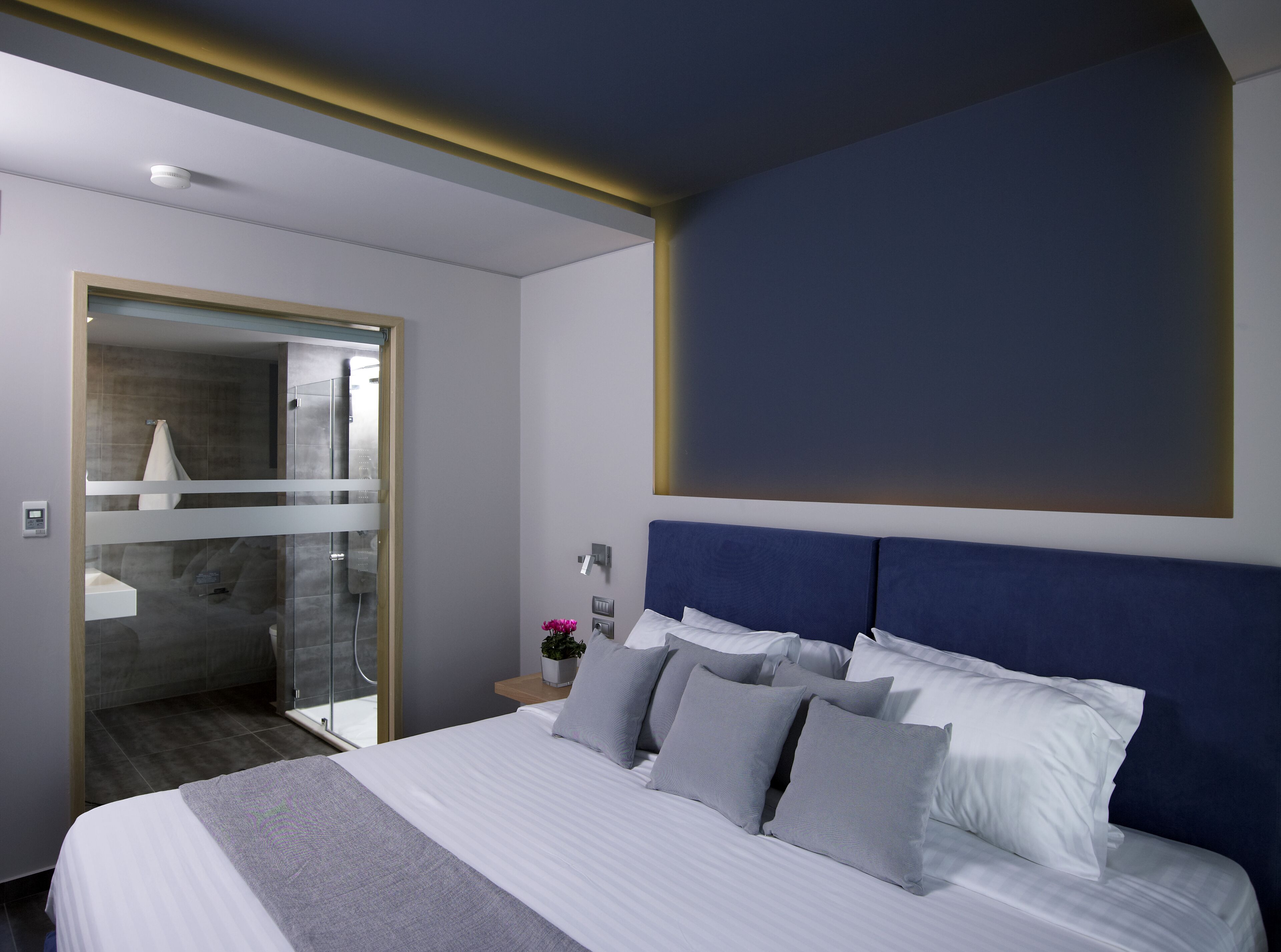 A modern hotel room with a large bed, a glass shower enclosure, and a view of the city.