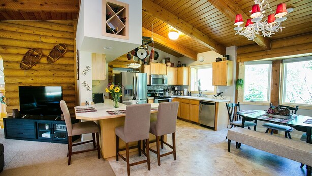 A spacious kitchen with wooden cabinets, a dining area with a bench, and a TV in the living area. - Nederland Getaway 4 Bedroom Home by RedAwning (Nederland)