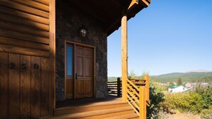 A wooden cabin with a stone wall entrance, a wooden porch, and a view of a town in the distance. - Nederland Getaway 4 Bedroom Home by RedAwning (Nederland)