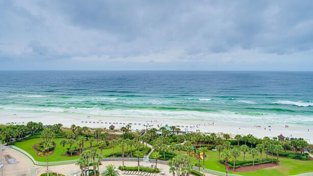 A beach resort with a well-maintained lawn, palm trees, and a view of the ocean. - St. Croix 1406 3 Bedroom Condo by RedAwning (Destin)
