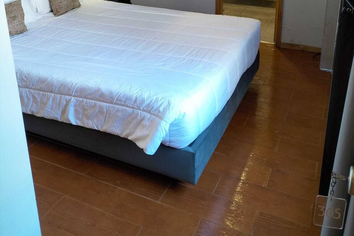 Een slaapkamer met een bed, nachtkastje, wandlamp en een zichtbare badkamer door een geopende deur.