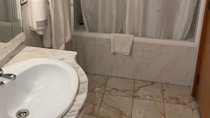 Une salle de bain avec un lavabo blanc, un miroir, un distributeur de serviettes et un rideau de douche.