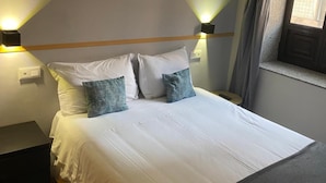 Un lit bien fait, avec du linge de lit blanc et deux oreillers, une table de chevet et deux lampes fixées au mur.