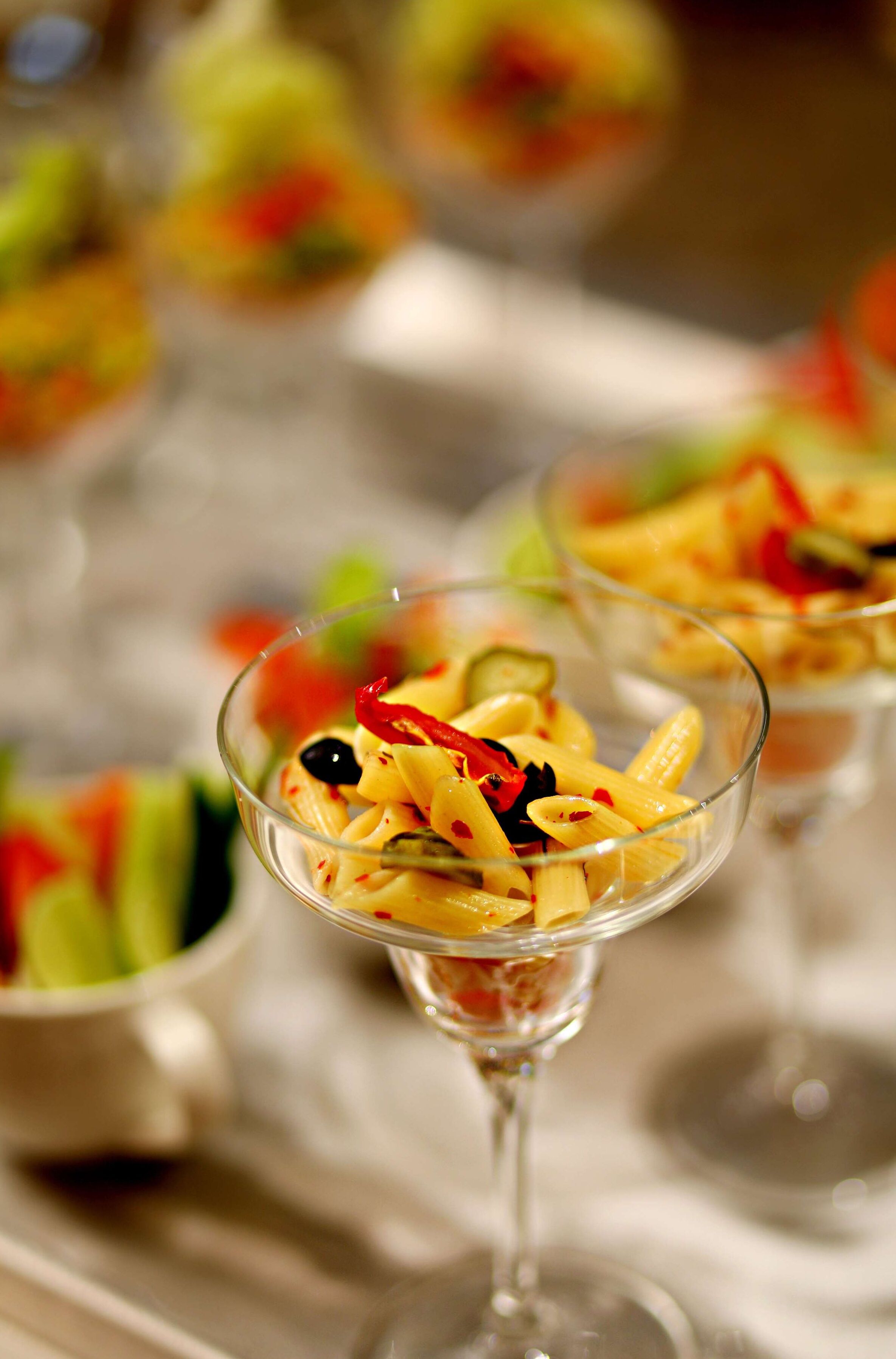 A glass bowl containing pasta with vegetables.