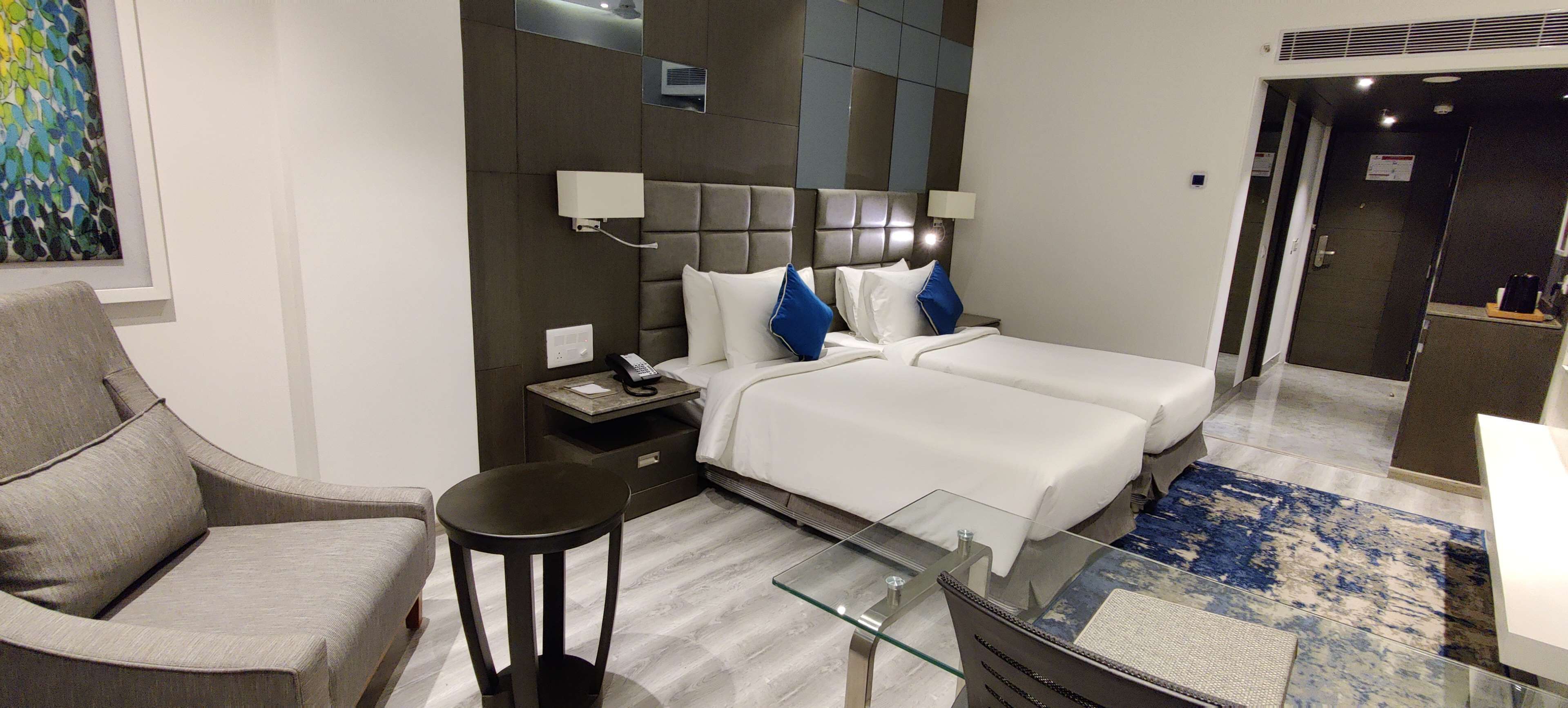 Una habitación de hotel moderna con una cama grande, un sofá, una mesita y una mesa de centro de vidrio.