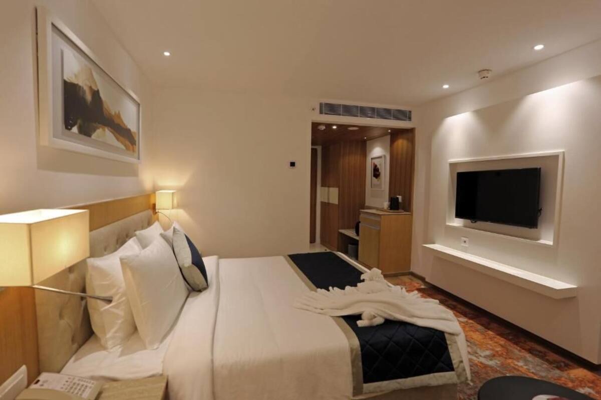 Une chambre d’hôtel comprenant un lit, une table de chevet, une lampe, une télévision et un petit bureau.