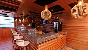 Una zona de bar con una barra alargada, varios taburetes y lámparas colgantes de madera.