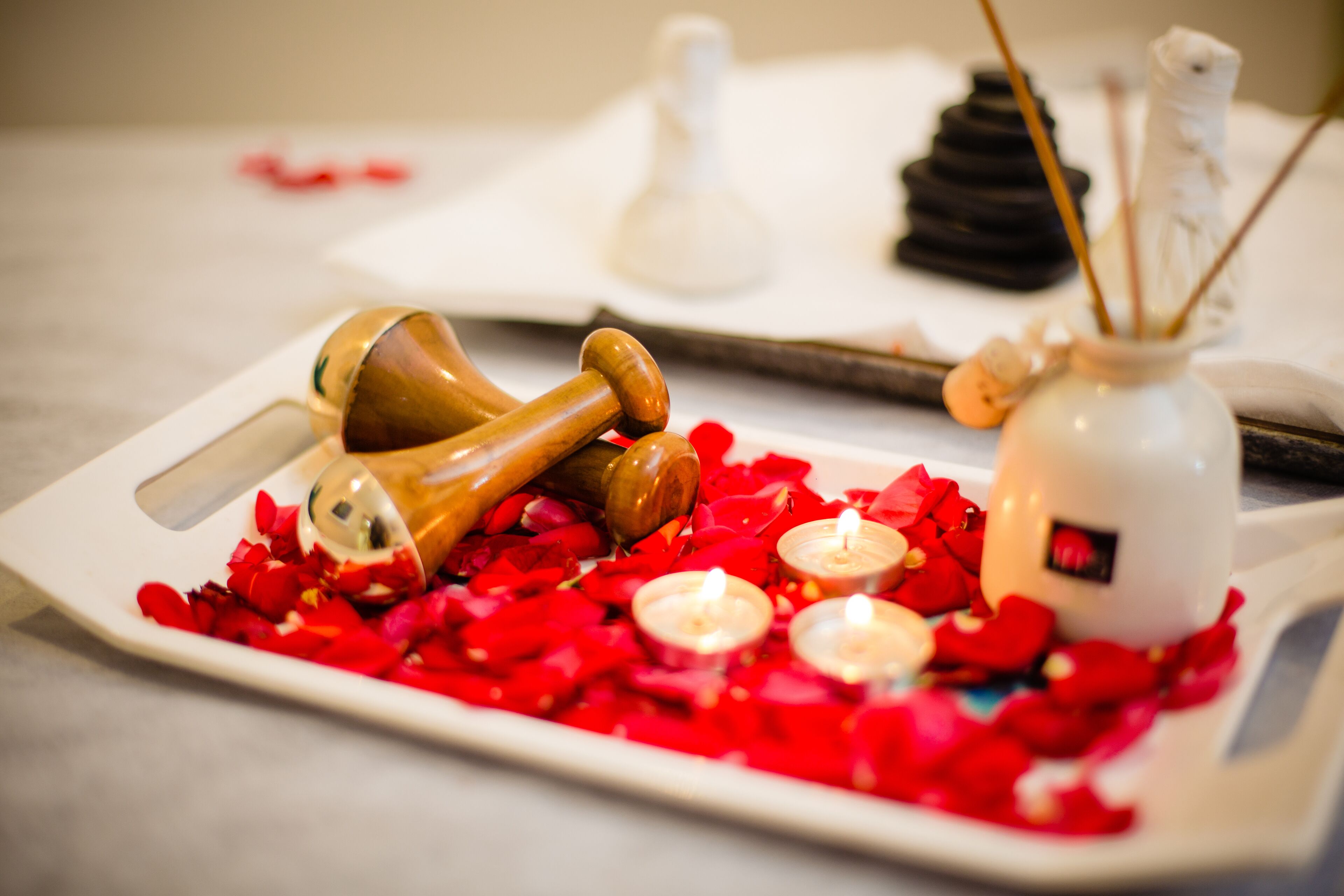 A tray with rose petals, candles, and a wooden object on a table.