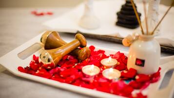 A tray with rose petals, candles, and a wooden object on a table.
