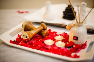 A tray with rose petals, candles, and a wooden object on a table.