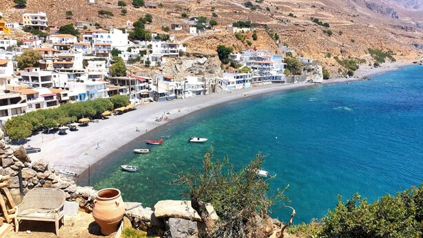 A coastal town with white buildings, a sandy beach, and clear blue sea.
