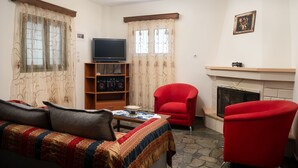 Ein Wohnzimmer mit einer Couch, roten Sesseln, einem Fernseher, einem Kamin und Vorhängen.