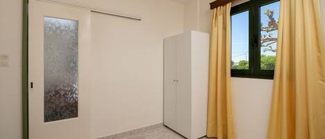 Quarto com porta de correr, guarda-roupa, cama com toalha branca enrolada e cortinas amarelas numa janela.