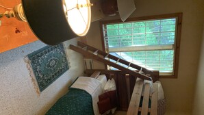 Una habitación pequeña y acogedora con una cama individual, ventana con persianas, una escalera de madera y una mesita.