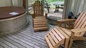 Una terraza de madera con un jacuzzi, dos sillas Adirondack y una mesa con una lámpara.