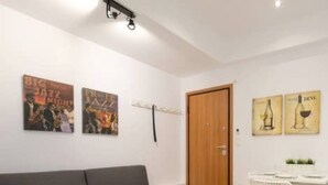 Ett modernt vardagsrum med en grå soffa, ett litet vitt bord och en matplats med ett vitt bord och stolar. På väggen hänger två affischer, en med ett jazzmotiv och en annan med vinglas.