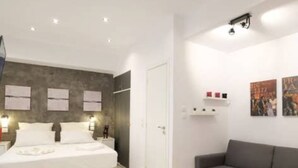 Ett modernt hotellrum med en säng, en grå soffa, ett litet bord och konst på väggen.