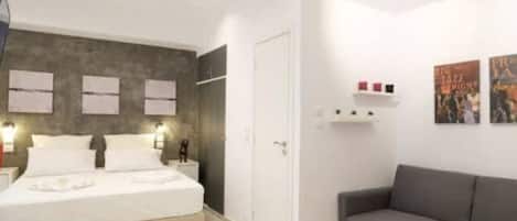 A modern hotel room with a bed, a gray sofa, a small table, and wall art.
