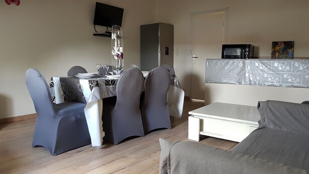 A dining area with a table set for four, a television mounted on the wall, and a microwave on a counter.