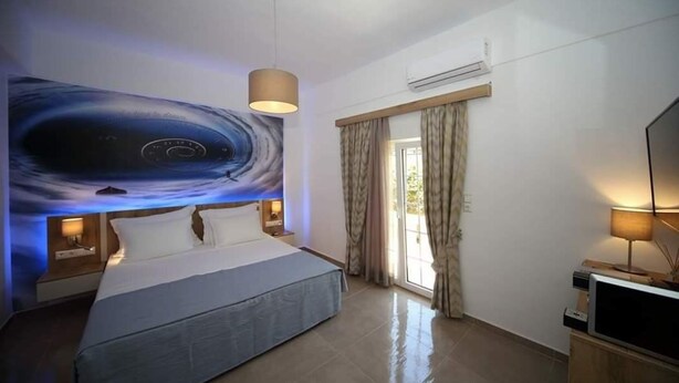 A modern hotel room with a large bed, a flat-screen TV, a ceiling light, and a window with curtains. - XDream Suite I (Hersonissos)