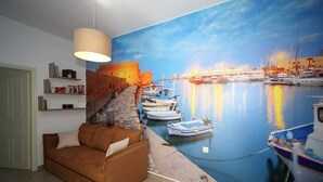 A living room with a mural of a harbor scene, a brown sofa, and a hanging light fixture. - XDream Suite I (Hersonissos)