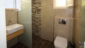 A modern bathroom with a built-in sink, a toilet, and a shower area. - XDream Suite I (Hersonissos)
