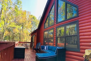 Una cabaña de troncos con terraza, ventanas amplias y un área de estar exterior azul.