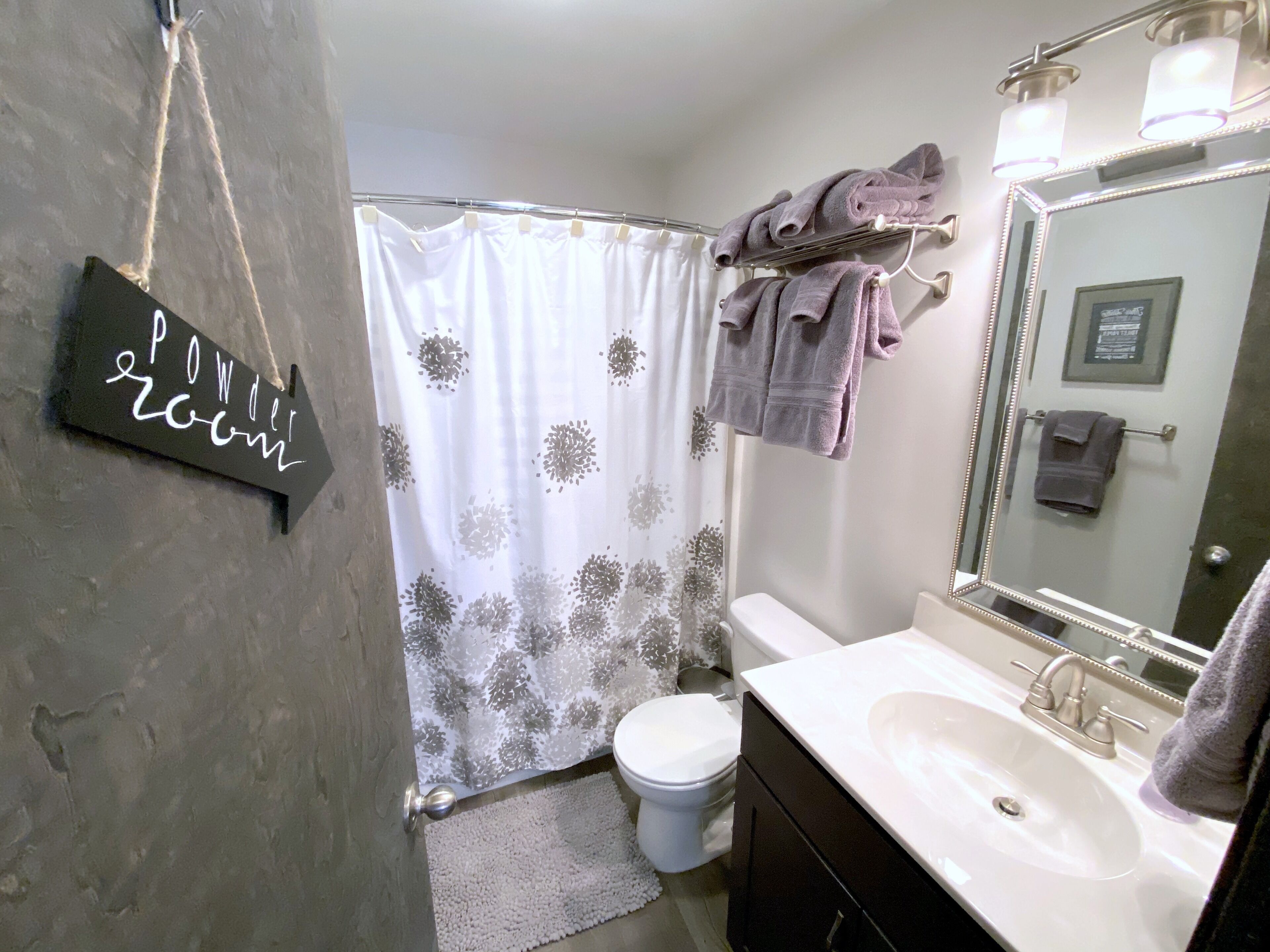 A bathroom with a white sink, a mirror, a toilet, a shower curtain, and towels hanging on a rack.