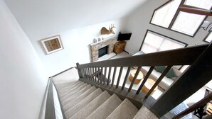 En trappa med ett träräcke leder upp till en liten plattform. På plattformen syns en öppen spis med en stenkamin och en väggmonterad tv.