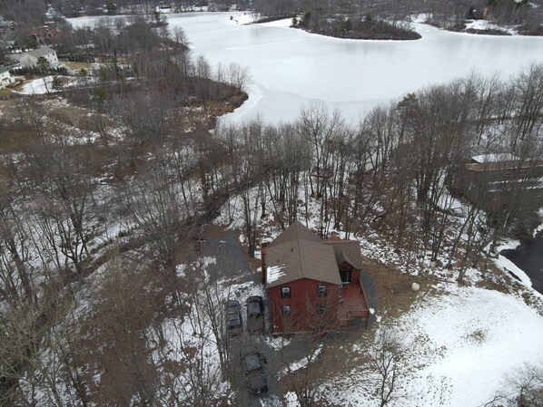Una casa roja con techo inclinado, rodeada de nieve y árboles sin hojas.