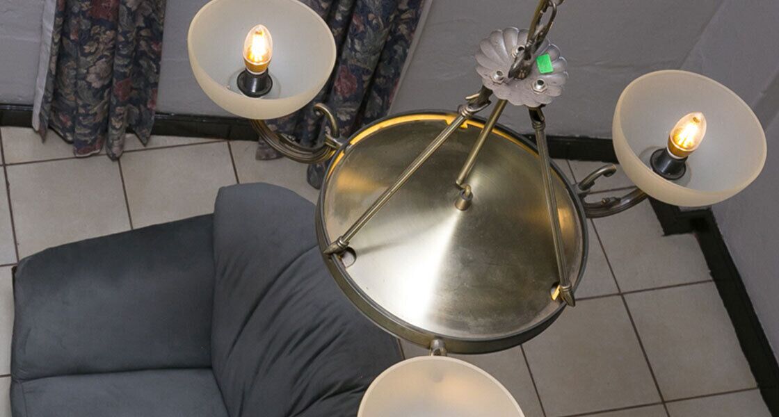 A ceiling-mounted chandelier with four light fixtures, a grey sofa, and a patterned curtain in the background.