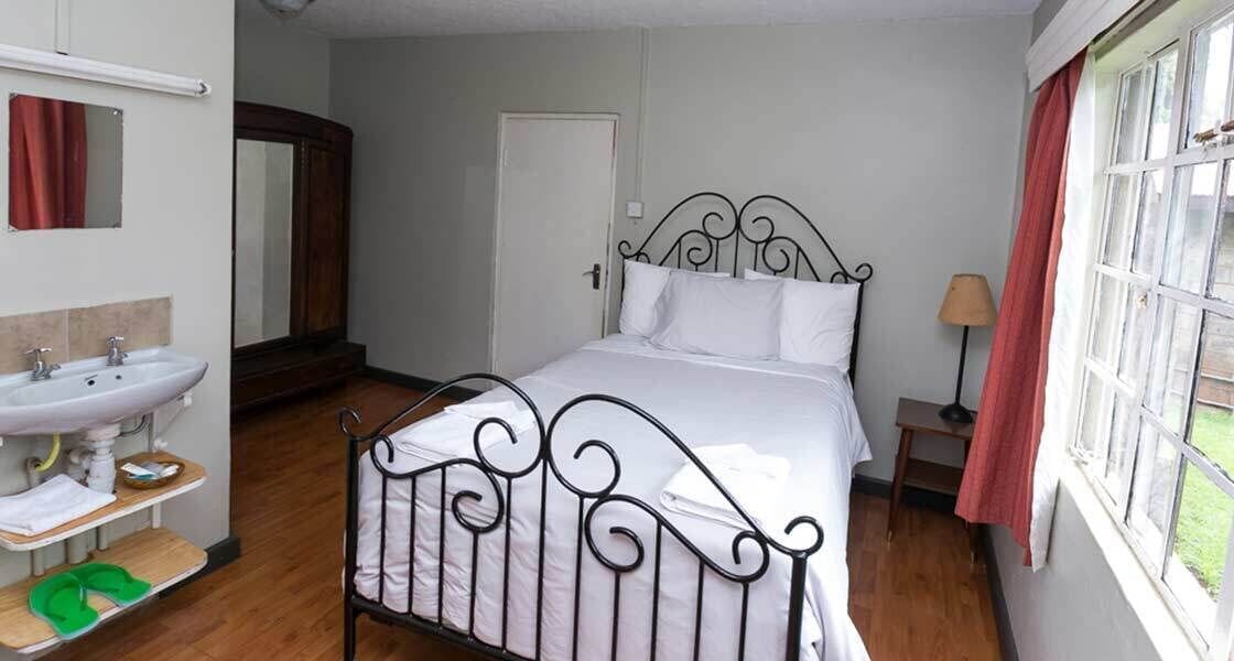 A bedroom with a bed, a bedside table, a lamp, a mirror, and a bathroom with a sink and mirror.