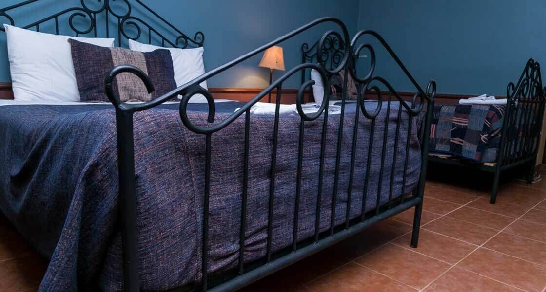 Un letto con struttura in metallo, una parete blu e un pavimento piastrellato.