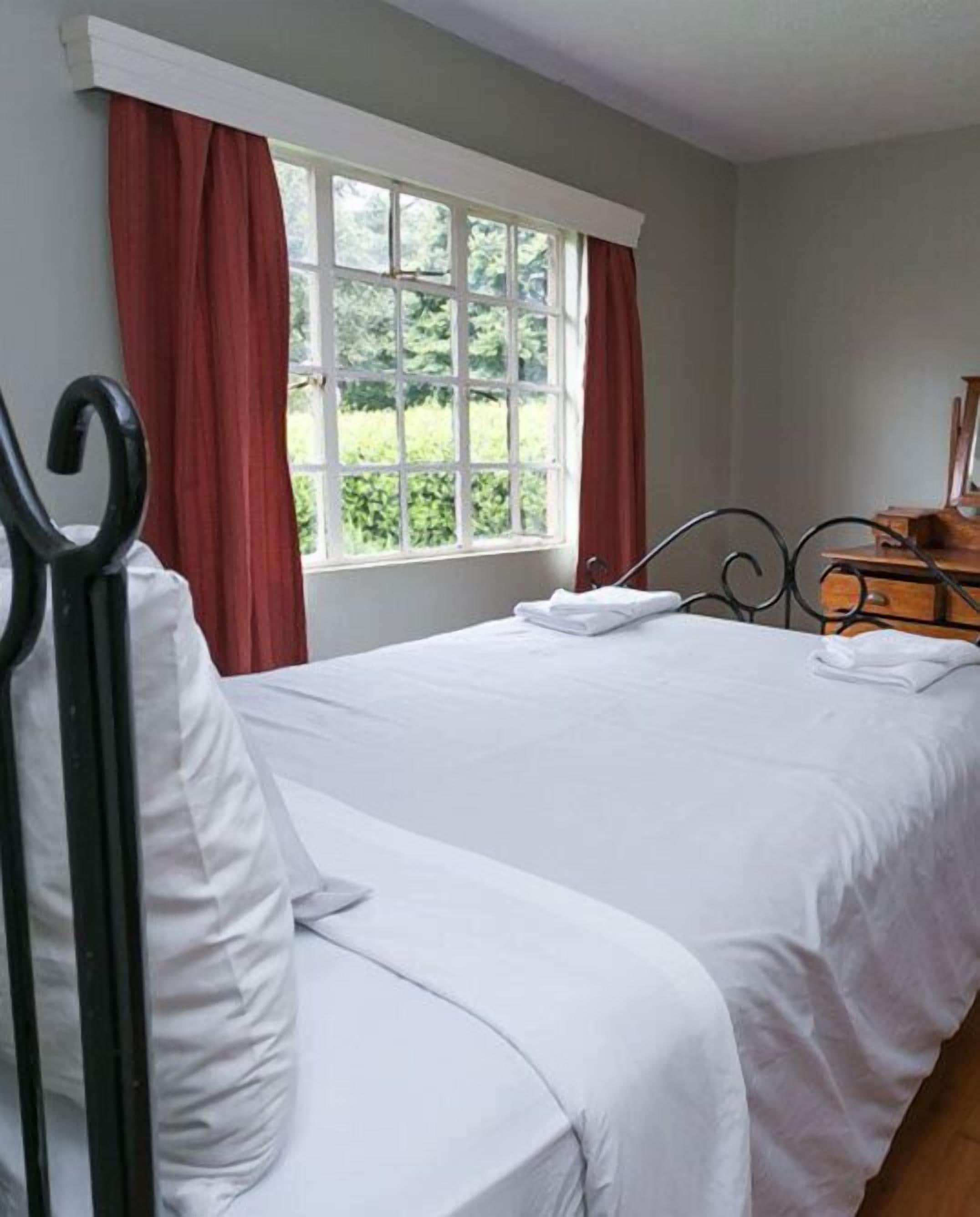 A bedroom with a bed, a dresser, and a window with curtains.