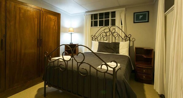 A bedroom with a metal bed frame, wooden wardrobe, and a bedside table with a lamp. - Brackenhurst Conference and Retreat Centre (Limuru)