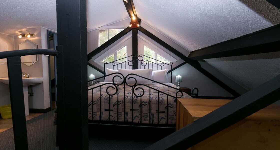 A bedroom with a sloped ceiling, a bed with a metal frame, a bedside table, and a window.