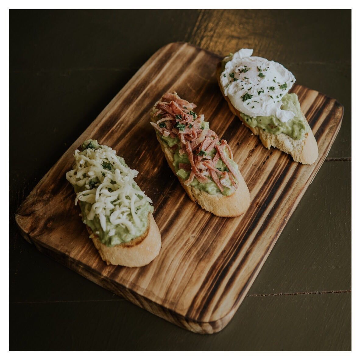 Tres sándwiches abiertos sobre una tabla de madera.