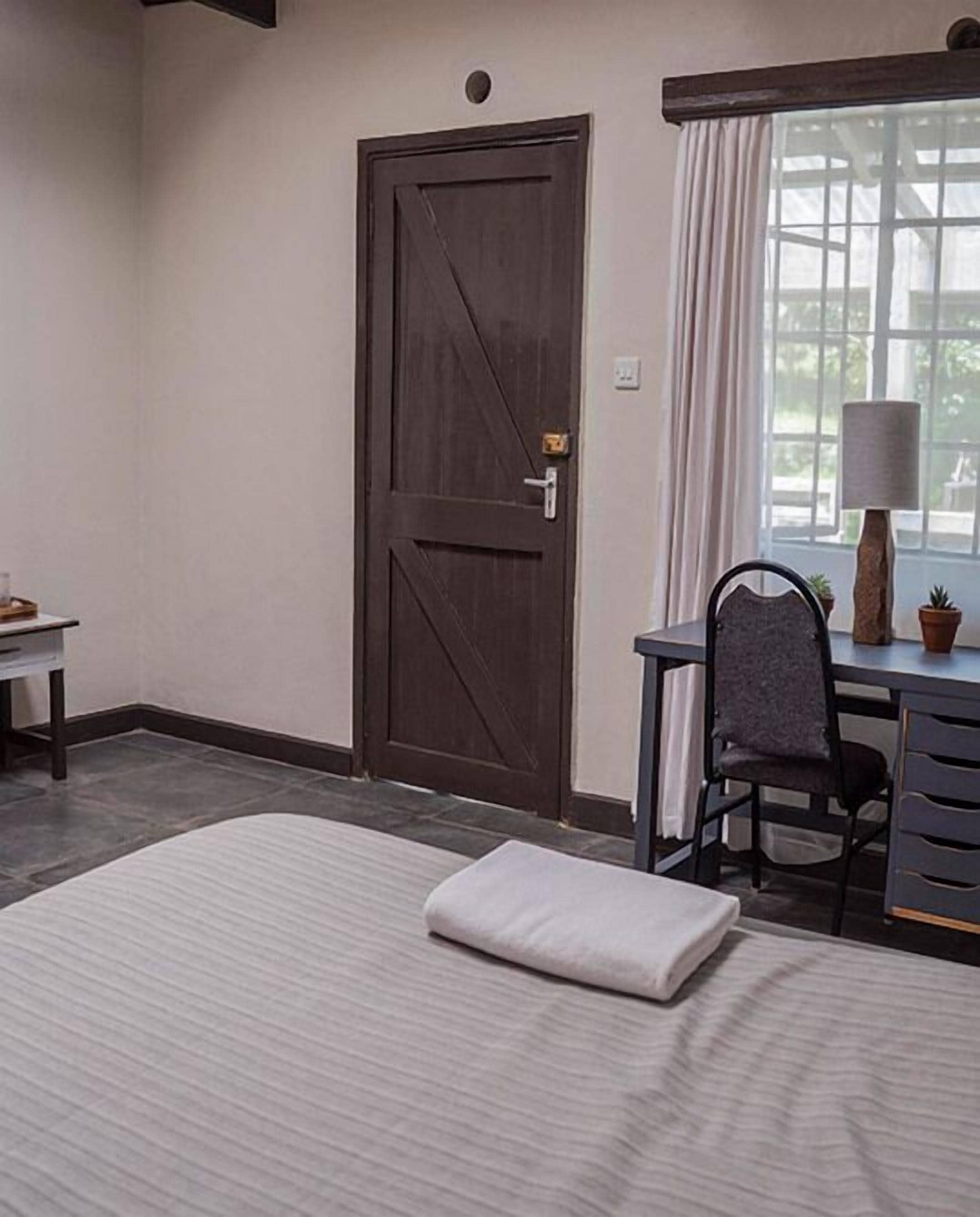 A bedroom with a bed, a desk, a chair, a window with curtains, and a door.