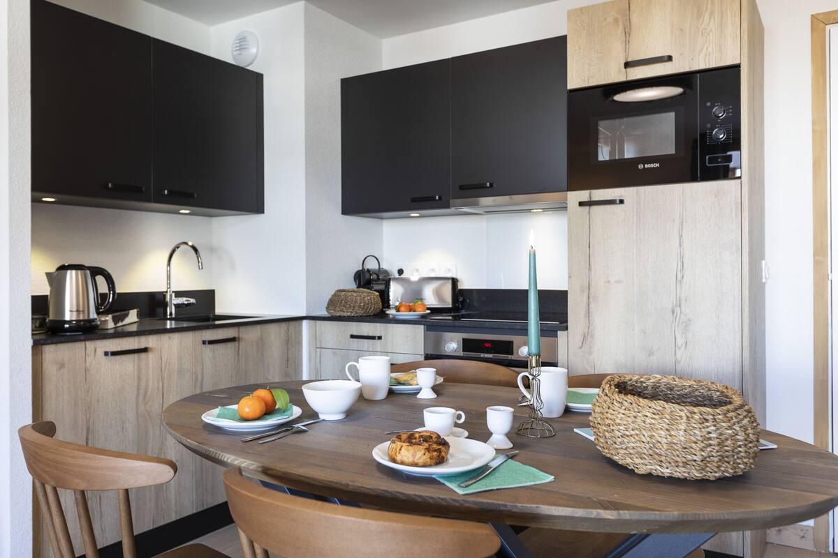 Een moderne keuken met donkere kastjes, een magnetron en een ronde eettafel met stoelen.