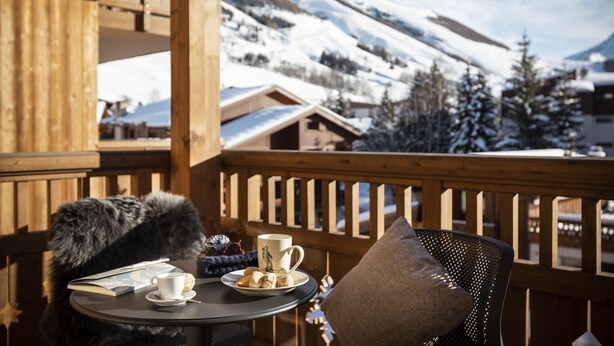 A wooden deck with a table set for a meal, a chair, and a view of snow-covered mountains.