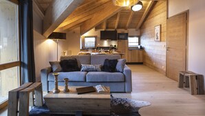 A cozy loft-style living area with a wooden ceiling, a grey sofa with cushions, a wooden coffee table, and a large window.