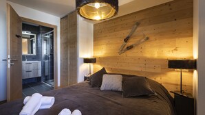 A modern bedroom with a wooden headboard, a large bed with dark bedding, two bedside lamps, and a mirror.