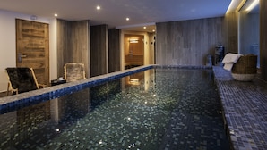 A modern indoor swimming pool with a wooden door, a bench, and a wicker basket.