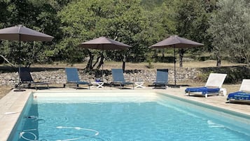 Relax by the serene pool surrounded by lush greenery and trees, with lounge chairs and umbrellas providing shade.