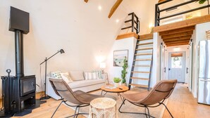Un salon chaleureux avec un canapé, deux fauteuils, une petite table, une cheminée et un escalier menant à l’ étage supérieur.