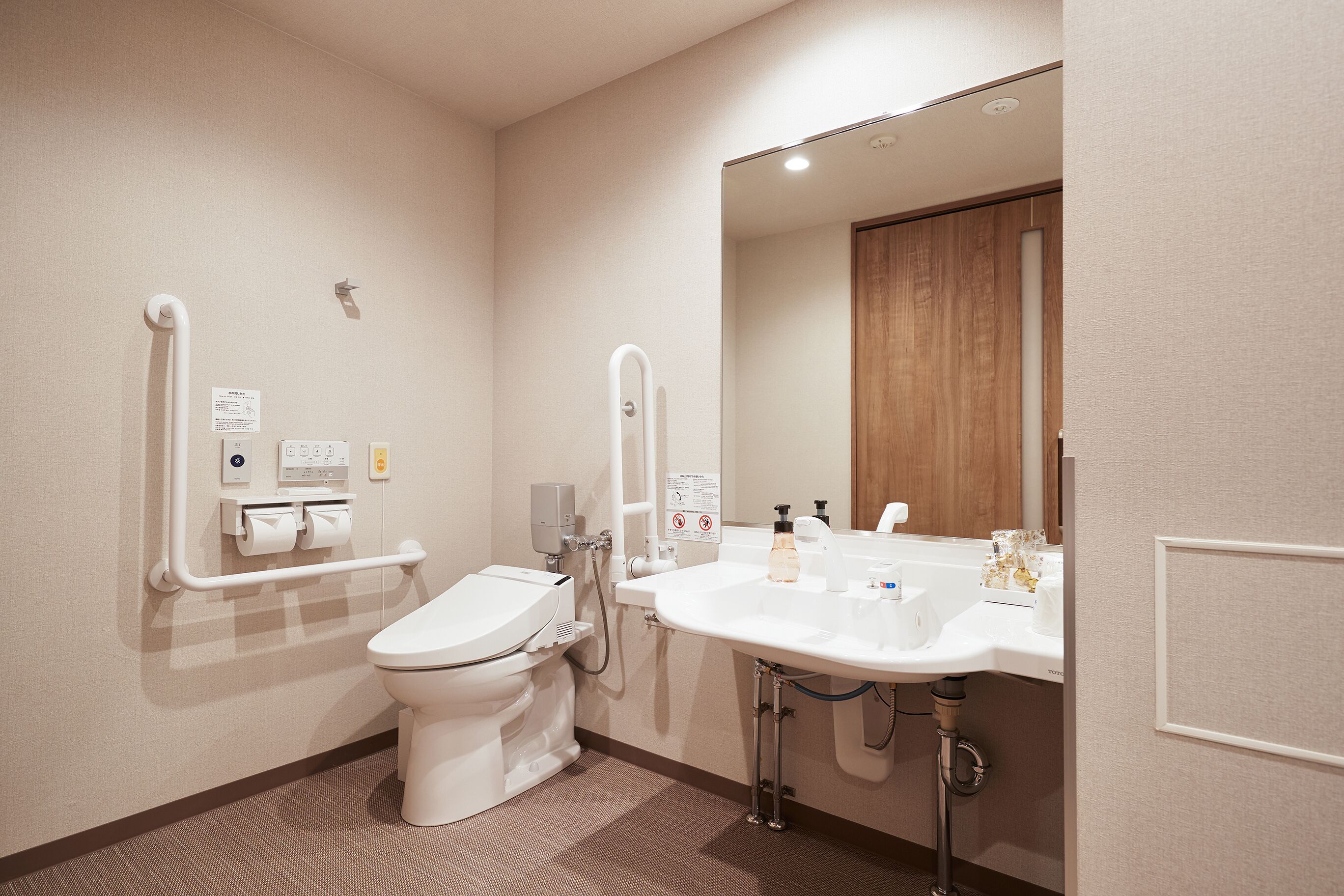 Une salle de bain moderne équipée de toilettes, de barres d’appui, d’un lavabo et d’un miroir.