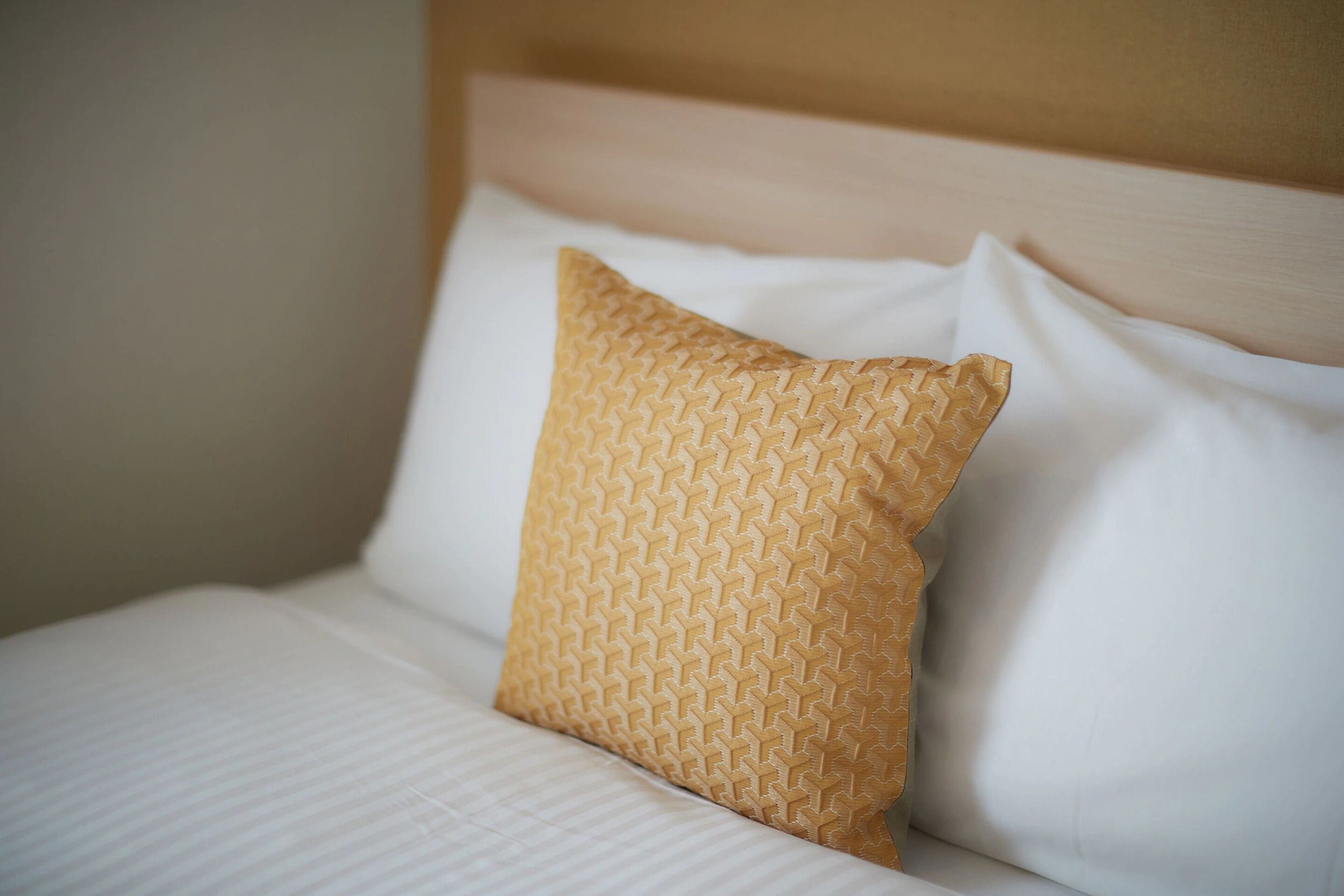 A bed with a patterned pillow and a plain white pillow.